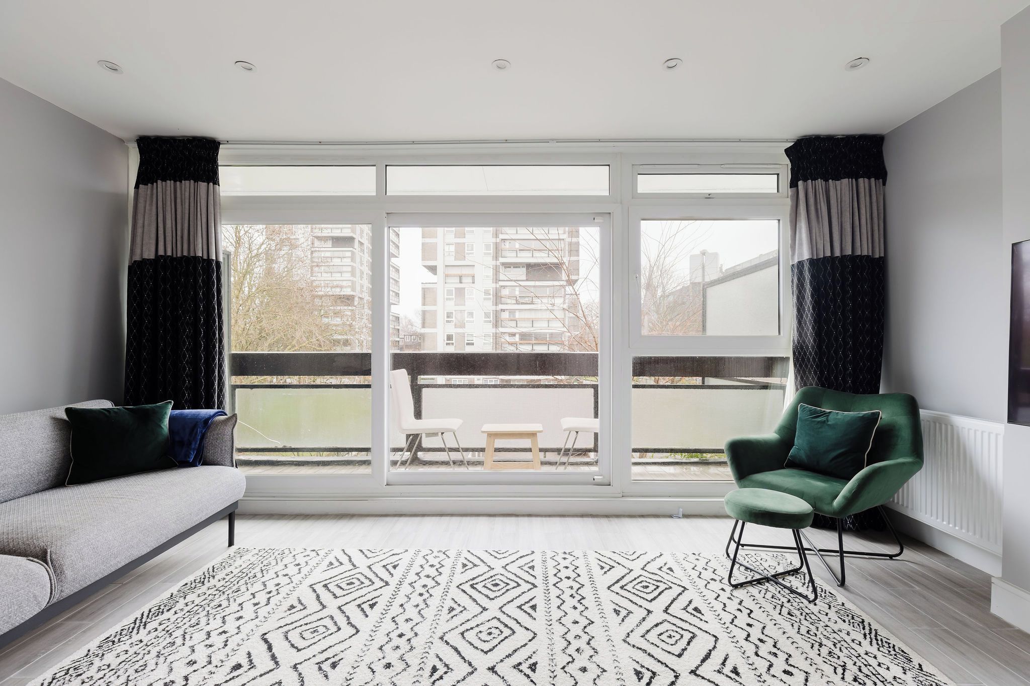 A modern living room with a grey sofa, a green armchair, and a patterned rug.