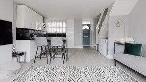 A modern kitchen with white cabinets, a dining area with two chairs, a grey sofa, and a patterned rug. - Contemporary 3BDR Retreat in South West London (Greater London)