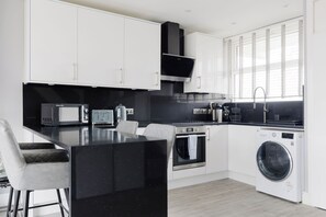 A modern kitchen with a central island, built-in appliances, and a washing machine. - Contemporary 3BDR Retreat in South West London (Greater London)