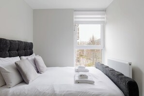 A bedroom with a bed, pillows, a radiator, and a window with a view. - Contemporary 3BDR Retreat in South West London (Greater London)