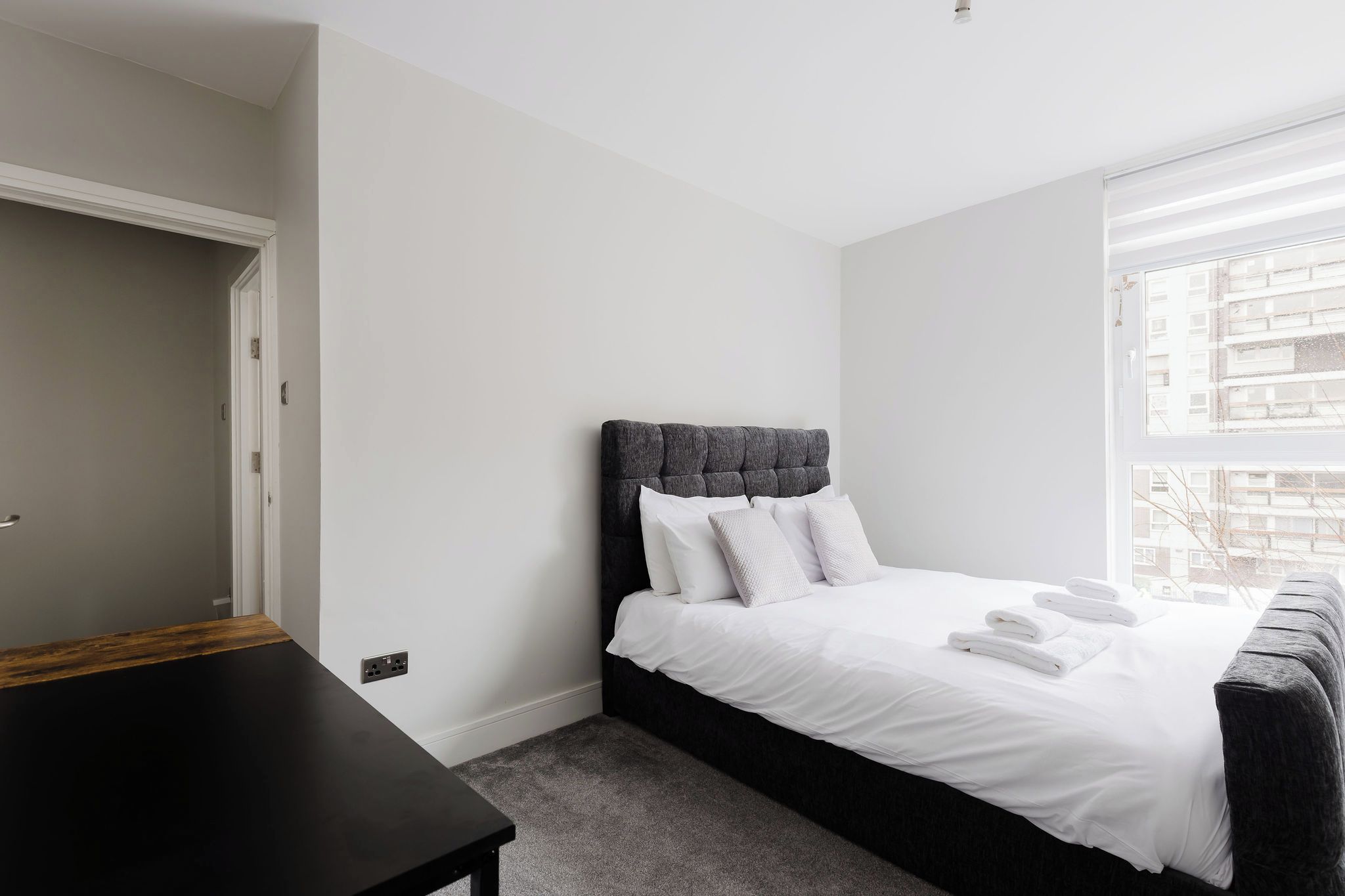 A bedroom with a bed, a bedside table, a window, and a door.