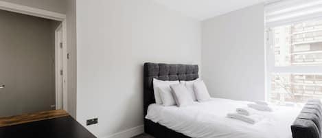 Een slaapkamer met een bed, nachtkastje, raam en deur.