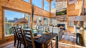 Un intérieur en bois avec une table à manger pour quatre personnes, une cheminée et de grandes fenêtres.