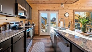 Une cuisine moderne avec des meubles de couleur sombre, des appareils électroménagers en acier inoxydable et une grande fenêtre.