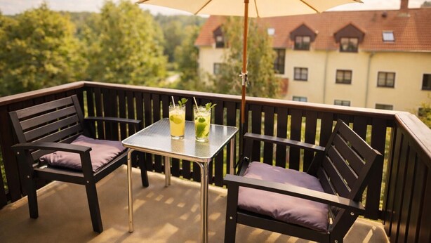 Een balkon met twee houten stoelen en een tafel, twee drankjes met lime en munt, en een grote parasol.