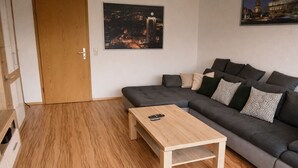 Een moderne woonkamer met een grijze bank, een houten salontafel en een stadsgezicht schilderij aan de muur.