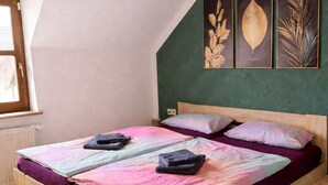 Een slaapkamer met een houten bed, een groene accentmuur en drie ingelijste botanische prints.