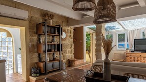 A spacious living area with a stone wall, wicker furniture, and a large window providing natural light. - Charming house in camargue private heated pool jacuzzi (Vauvert)