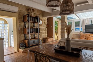 A spacious living area with a stone wall, wicker furniture, and a large window providing natural light. - Charming house in camargue private heated pool jacuzzi (Vauvert)