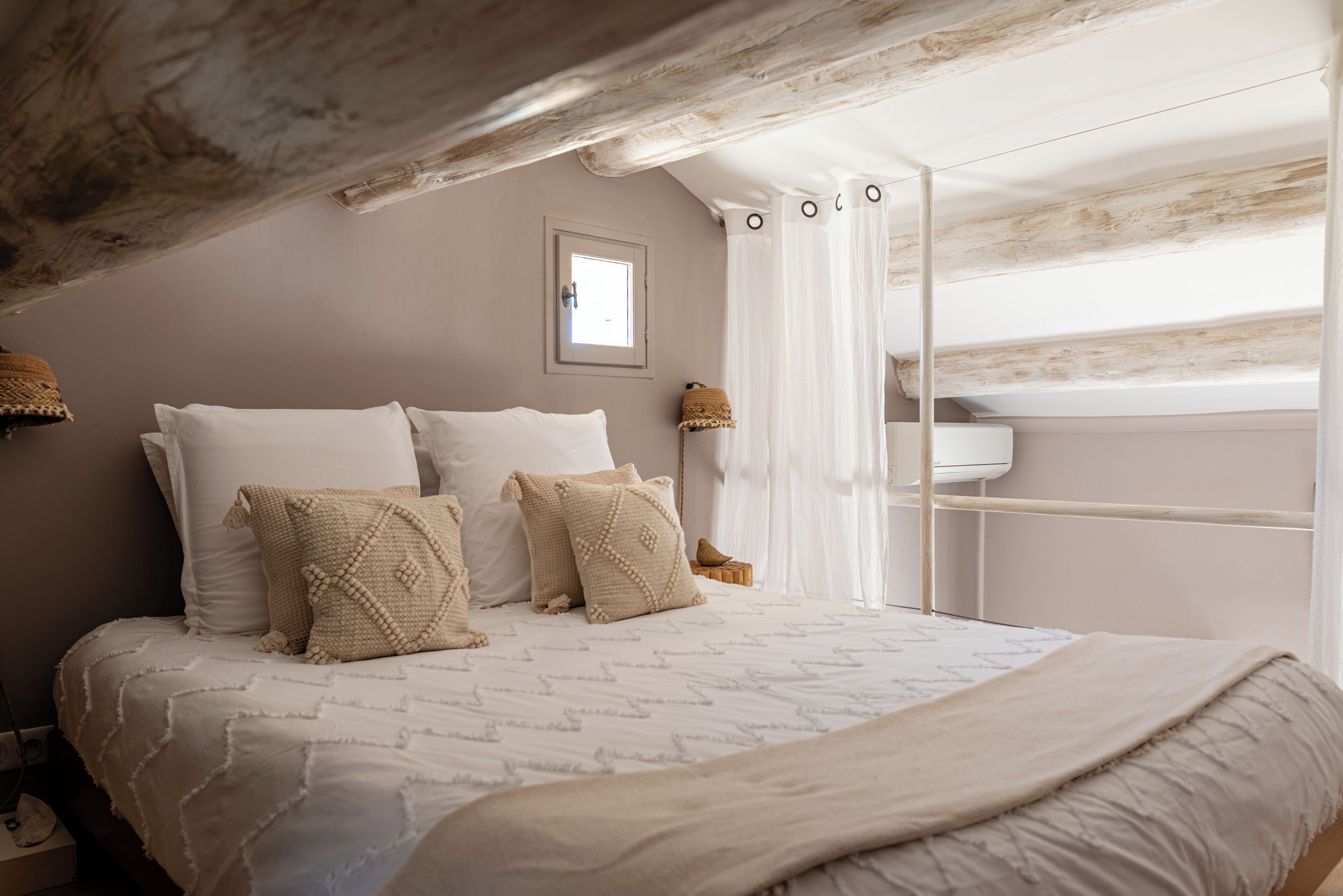 Ein Schlafzimmer mit einem großen Bett, einem kleinen Fenster und einer Holzbalkendecke.