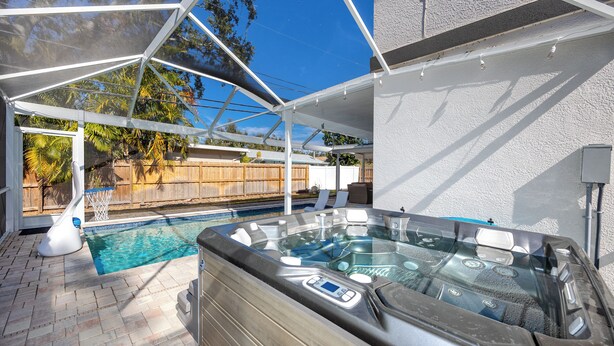 Ein Whirlpool mit Bedienfeld, ein Schwimmbecken und eine überdachte Terrasse mit Holzzaun im Hintergrund.