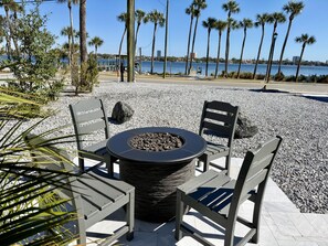 An outdoor seating area with a round table and two chairs, surrounded by pebbles and palm trees, overlooking a body of water. - The Stillwater - Pool, Riverfront & Viewing Dock - Close to Speedway & Downtown! (Daytona Beach)