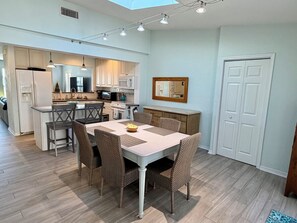 A modern kitchen with white cabinets, a dining area with wicker chairs, and a large mirror above the door. - The Stillwater - Pool, Riverfront & Viewing Dock - Close to Speedway & Downtown! (Daytona Beach)