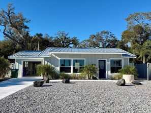 A modern two-story house with a metal roof, large windows, and a gravel driveway. - The Stillwater - Pool, Riverfront & Viewing Dock - Close to Speedway & Downtown! (Daytona Beach)
