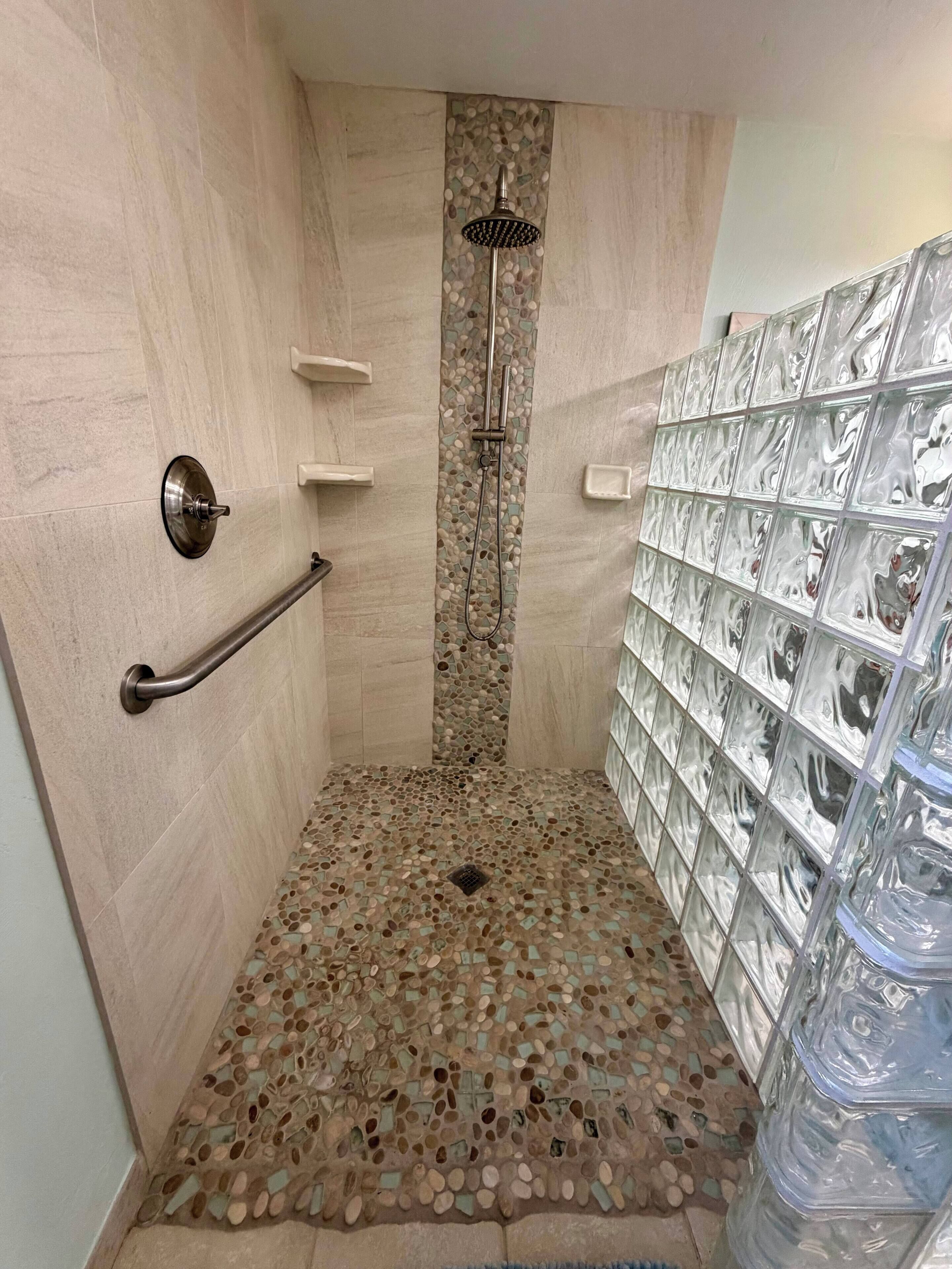 A shower with a mosaic floor, a glass shower enclosure, and a tiled wall with a decorative pattern.