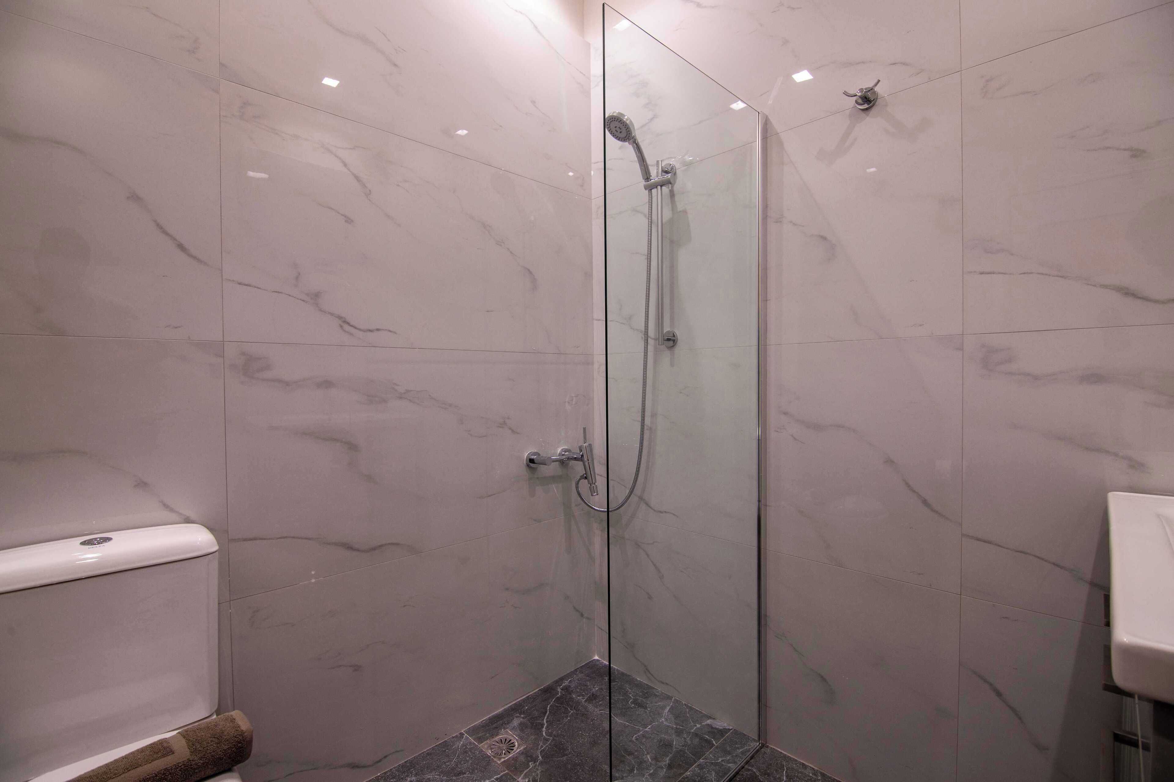 A glass-enclosed shower with a handheld showerhead and a wall-mounted faucet.