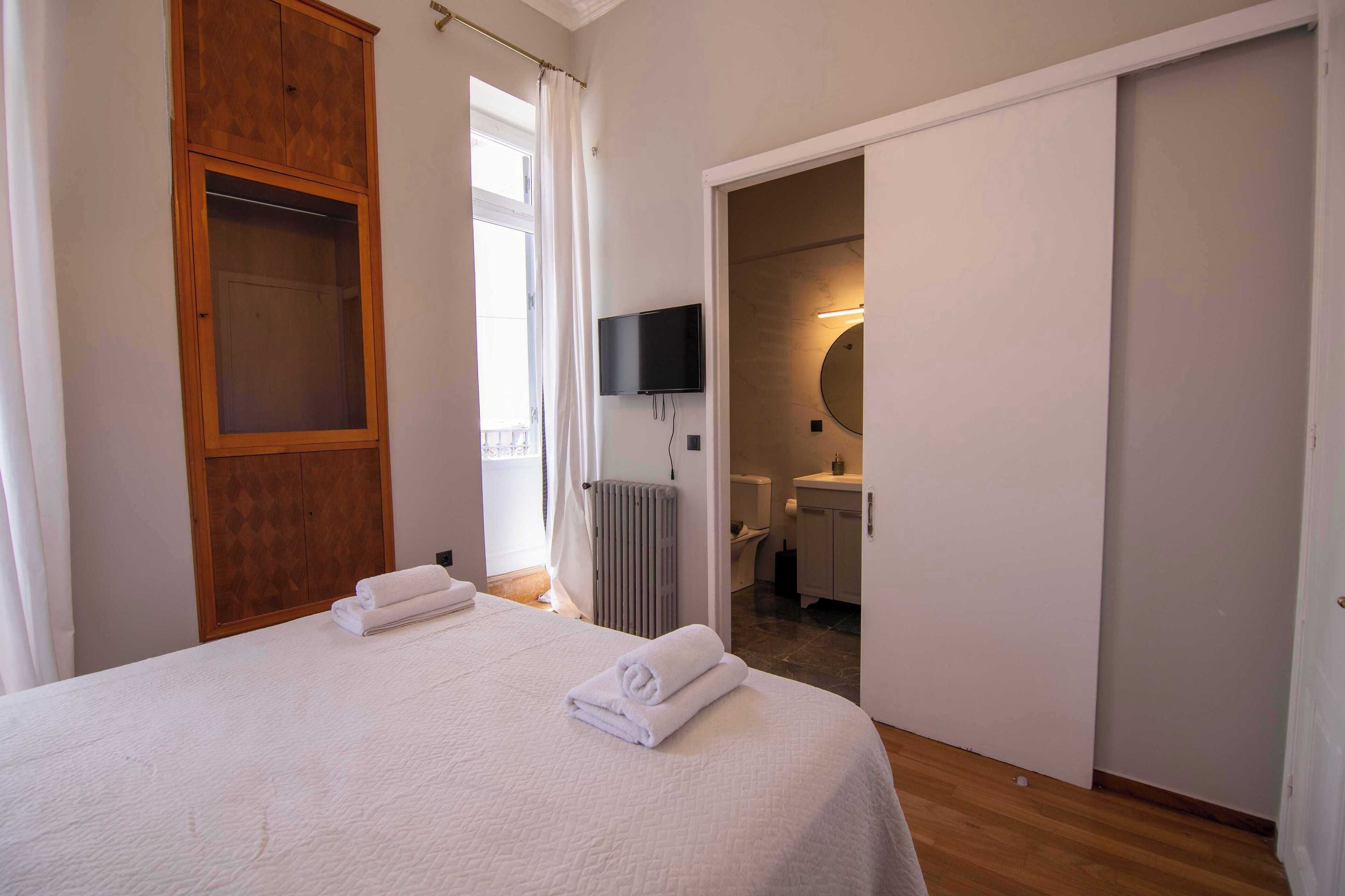 Une chambre d’hôtel avec un lit, une armoire en bois, un téléviseur et une salle de bain visible à travers une porte ouverte.
