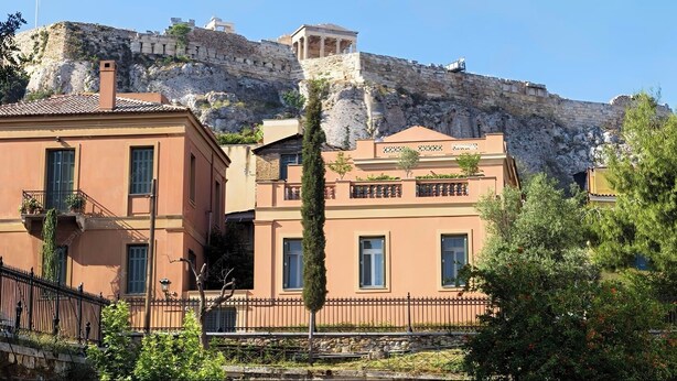 Un edificio con pared de piedra y vista a una colina rocosa.