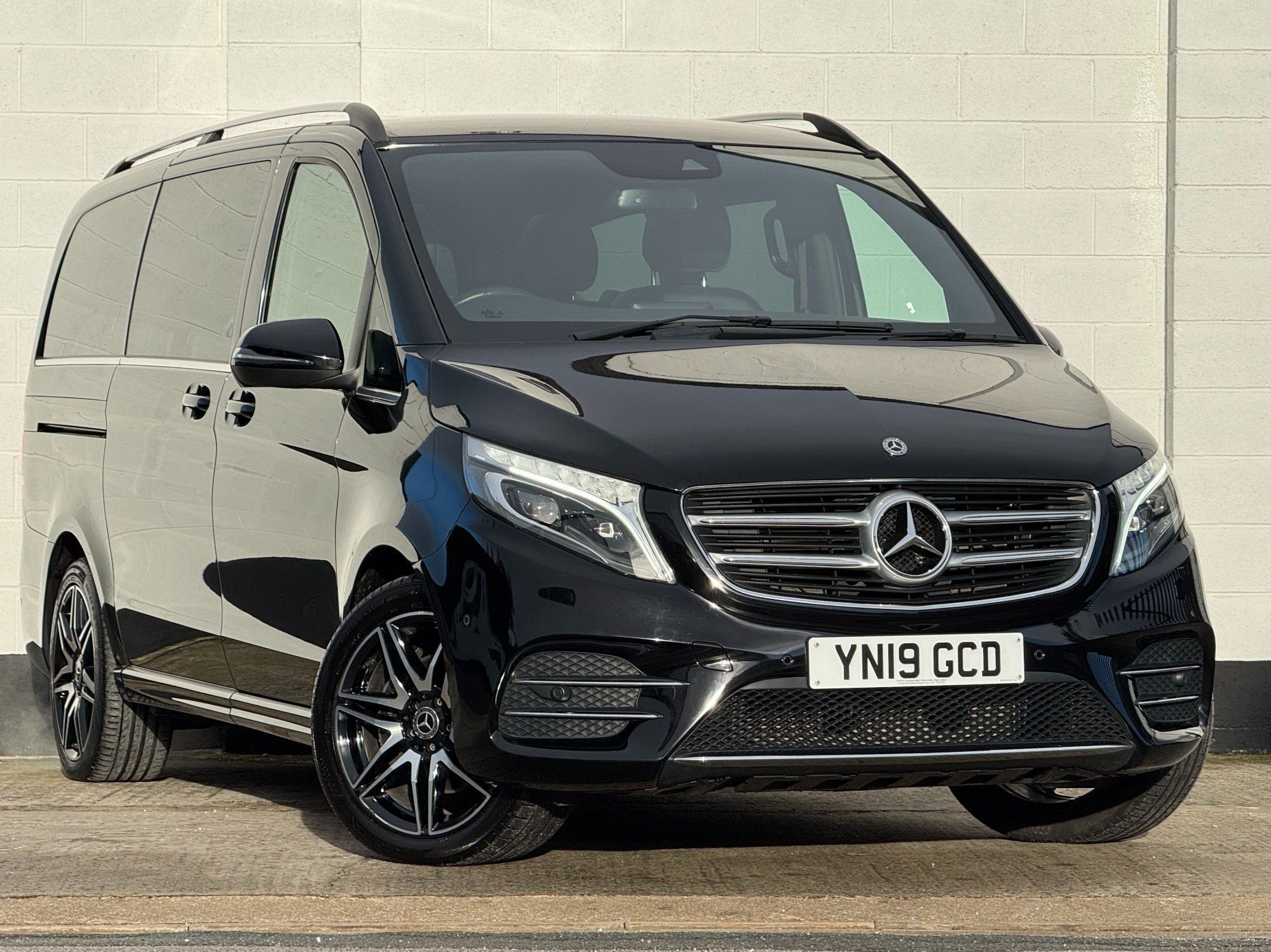 A black Mercedes-Benz van parked in front of a white brick wall.