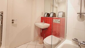 Un baño con puerta blanca, zona de ducha con azulejos rojos, lavabo blanco y un inodoro.