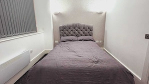 Una habitación pequeña y estrecha con una cama individual, una ventana con persianas y un radiador.