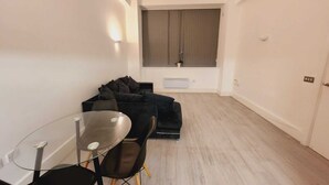 Una sala de estar moderna con una mesa de vidrio, un sofá negro y un ventanal con cortinas.