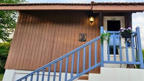 A wooden building with a blue staircase, a door, and a small porch with a planter.