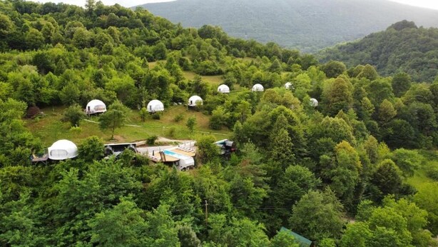 A cluster of dome-shaped yurts in a forested area with a view of a mountain range in the background. - Glamping Georgia - Krikhi  (Ambrolauri)