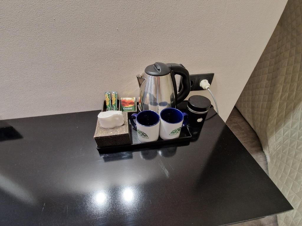 Una mesita con un hervidor, dos tazas, una caja de pañuelos y un paquete de pañuelos.
