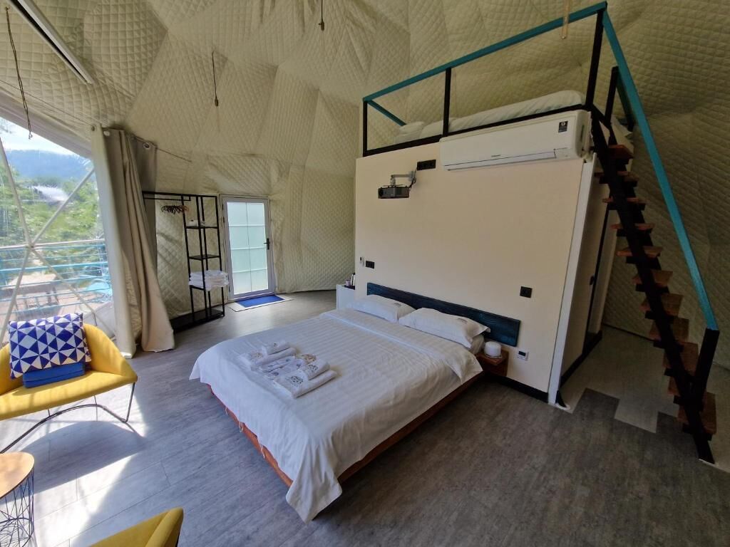 A bedroom with a bed, a chair, a small table, and a staircase.