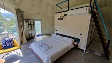 A bedroom with a bed, a chair, a small table, and a staircase.