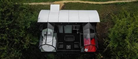 An aerial view of a modern, compact house with a flat roof, a central living area with a sofa and a dining table, and a red object on the right side.