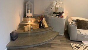 Un soggiorno accogliente con una scala a chiocciola, un lanternino bianco, un tavolino con candele, una bottiglia e un libro.