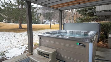 A hot tub under a covered area with a step for access, surrounded by a snowy landscape and trees.