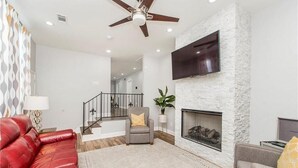 A modern living room with a fireplace, a red leather sofa, a grey armchair, and a ceiling fan. - Lovely, spacious & peaceful 3-bedroom house in New Orleans w AC & outdoor space. (New Orleans)