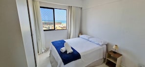 Hotelkamer met een bed, een raam met uitzicht op gebouwen, een nachtkastje en een lamp.