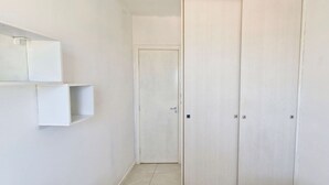 Un couloir avec une porte blanche, une petite étagère et un sol carrelé.