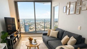 A modern living room with a large window, a sofa, a coffee table, and a TV. - Skyline Sanctuary | L35 Bay & City Views (Southbank)