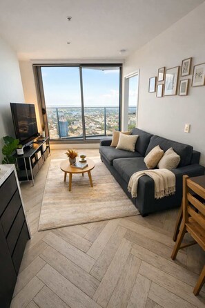 A modern living room with a large window, a sofa, a coffee table, and a TV. - Skyline Sanctuary | L35 Bay & City Views (Southbank)