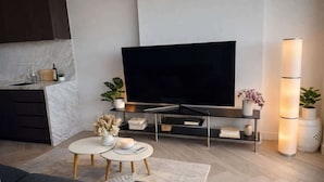 A modern living room with a flat-screen TV, a coffee table, a sofa, and a kitchen area with a marble backsplash. - Skyline Sanctuary | L35 Bay & City Views (Southbank)