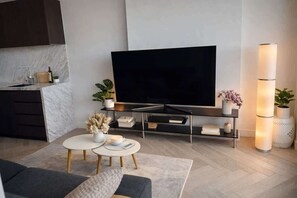 A modern living room with a flat-screen TV, a coffee table, a sofa, and a kitchen area with a marble backsplash. - Skyline Sanctuary | L35 Bay & City Views (Southbank)