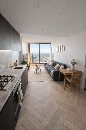 A modern kitchen with a gas stove, a dining area with a table and chairs, a sofa, and a large window offering a city view. - Skyline Sanctuary | L35 Bay & City Views (Southbank)