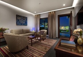 Una sala de estar moderna con sofá, sillón y mesa de centro, un cuadro en la pared y vistas a través de un ventanal.