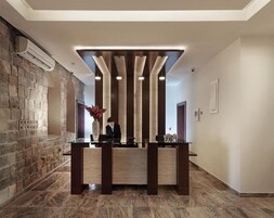 Un mostrador de recepción con un fondo de pared de piedra, un jarrón de flores y un elemento de iluminación moderno en el techo.