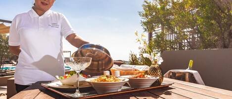 A person serving food at an outdoor table with a tray, a glass, and a bowl of salad.