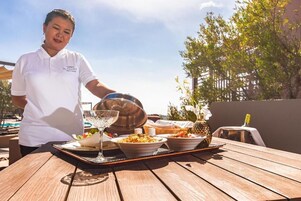 Una persona sirviendo comida en una mesa al aire libre, con una bandeja, un vaso y un tazón de ensalada.