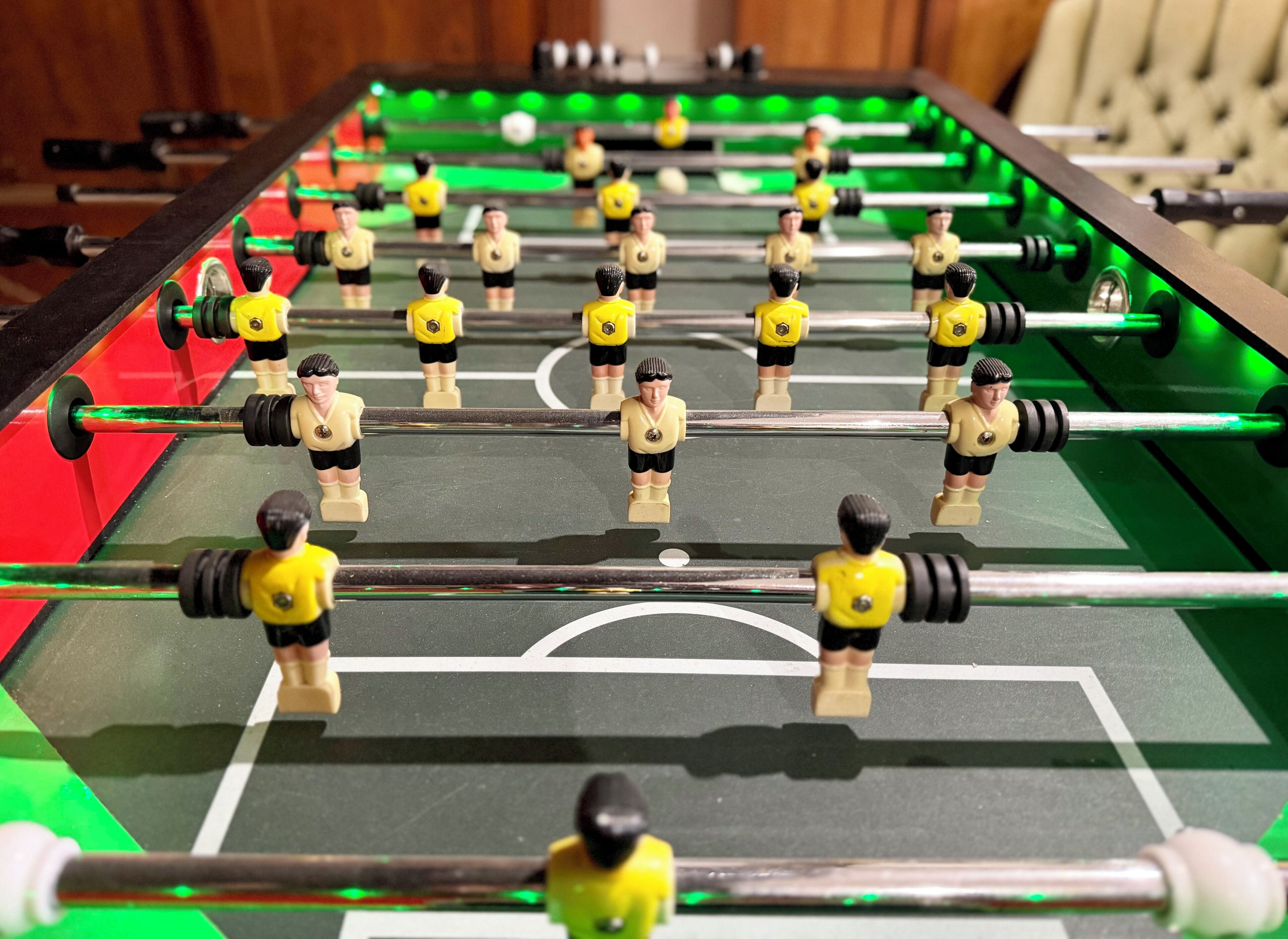Una mesa de fútbol de mesa con varios jugadores y palos, sobre un campo verde con líneas blancas.