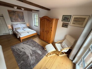 Un dormitorio con cama, armario de madera, dos mecedoras, alfombra y cuadros en la pared.