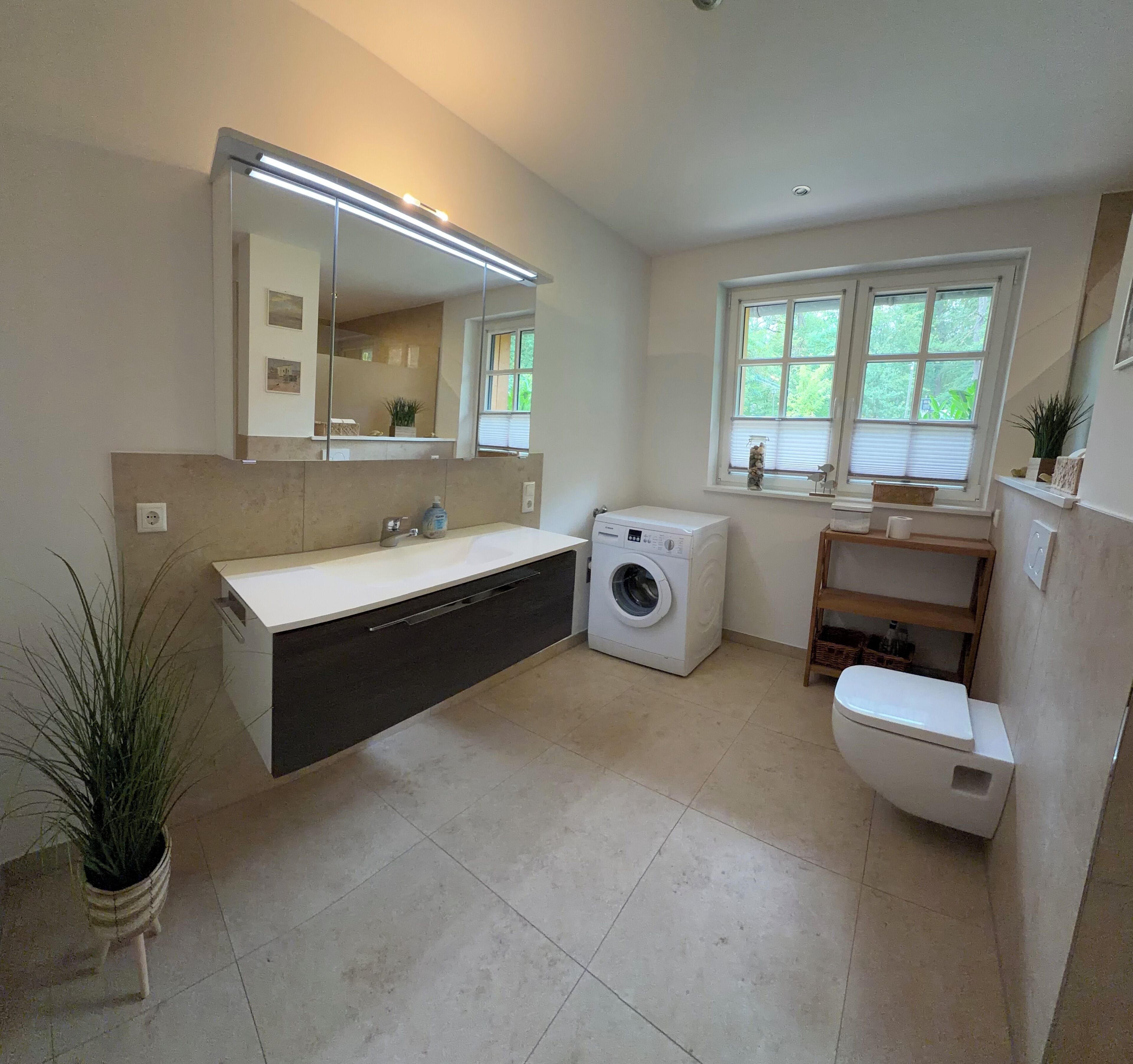 Ein modernes Badezimmer mit Waschmaschine, Toilette, Waschbecken mit Spiegel und einem Fenster für natürliches Licht.