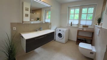 Ein modernes Badezimmer mit Waschmaschine, Toilette, Waschbecken mit Spiegel und einem Fenster für natürliches Licht.